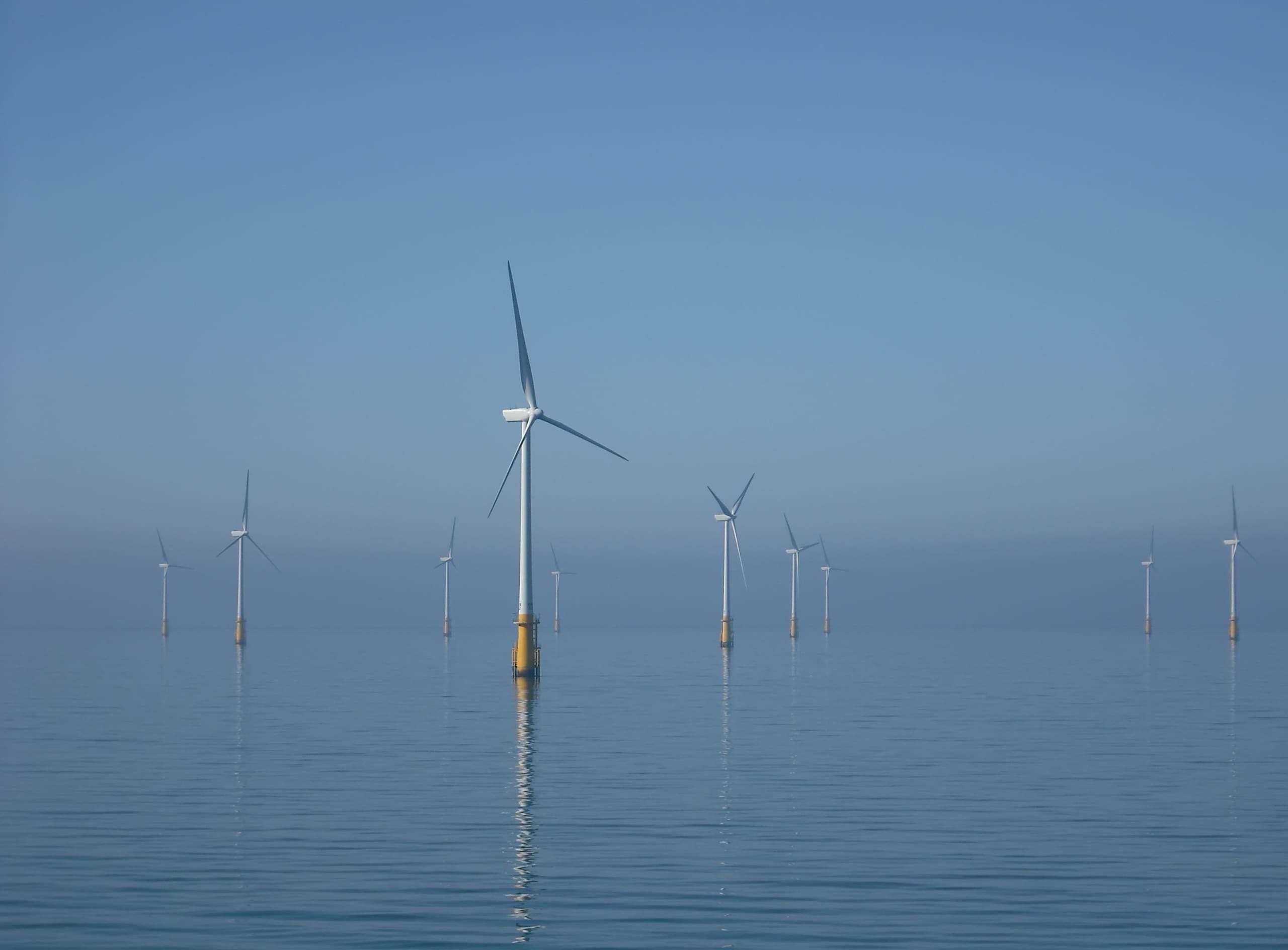 Offshore wind turbines standing in a calm, hazy sea